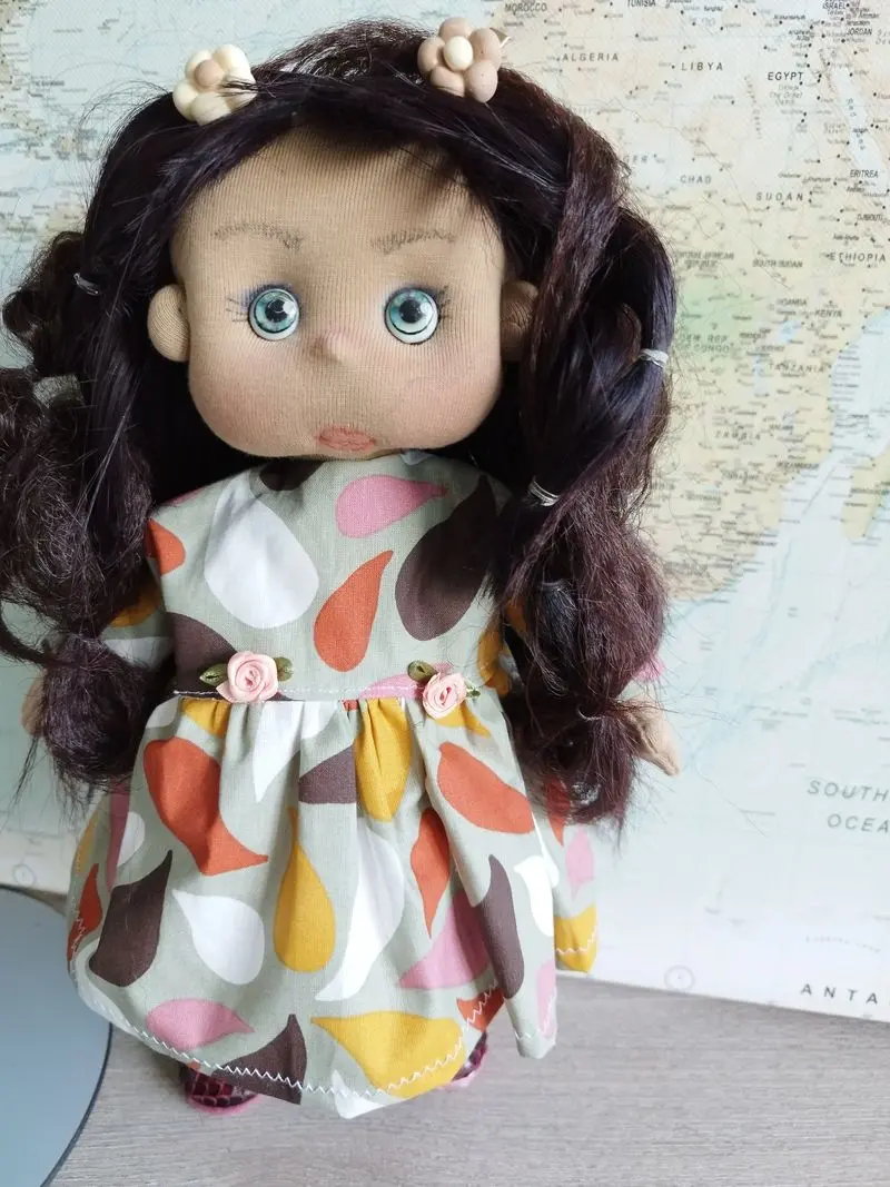 Muñeca de tela artesana Maryxeniss: muñeca de tez morena con pelo negro en trencitas, ojos azul claro y vestido estampado.