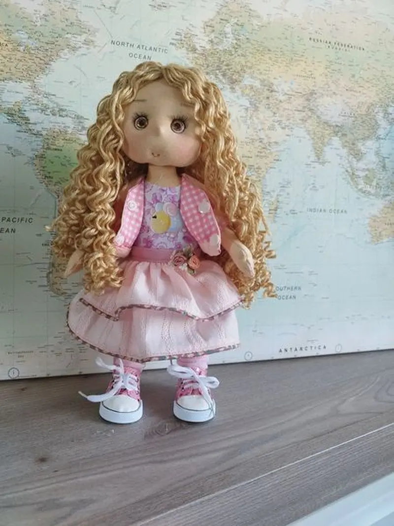 Bienvenida al catálogo de Maryxeniss muñecas artesanas de tela: taller con muñeca de pelo largo rubio, vestido rosa con volantes y chaqueta reversible.