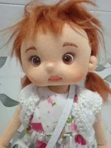 Primer plano de mu&ntilde;eca de tela articulada soft con ojos casta&ntilde;os, pelo rojizo alborotado.