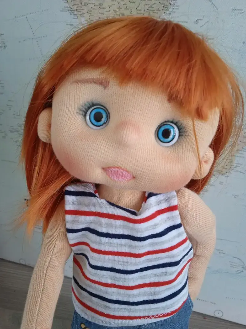 Primer plano del rostro de la muñeca de tela artesana con pelo pelirrojo, ojos azules.