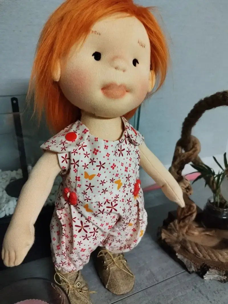 Primer plano del peto con motivos estampados y los zapatos marrones de la muñeca de trapo.