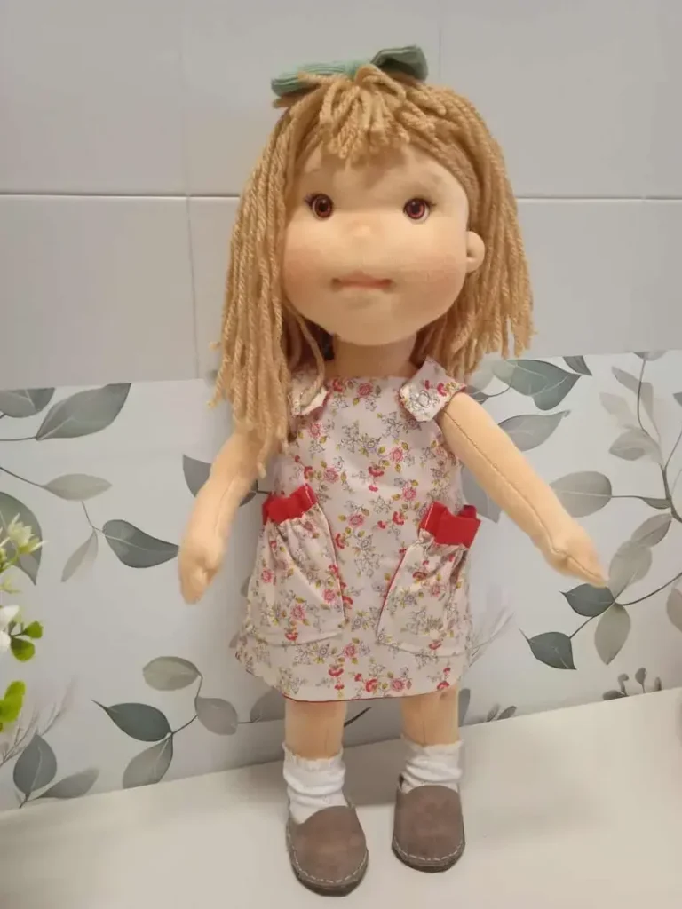 Mu&ntilde;eca Waldorf artesanal de tela con media melena marr&oacute;n arena y vestido estampado con bolsillos.