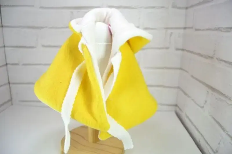 Ropa para muñeca de tela artesana Maryxeniss: capa de color amarillo forrada de borreguito blanco en un perchero.