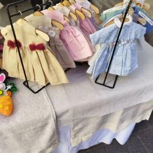 Colecci&oacute;n de vestidos artesanales para mu&ntilde;ecas de tela de Maryxeniss colgados en dos burros de ropa en miniatura.
