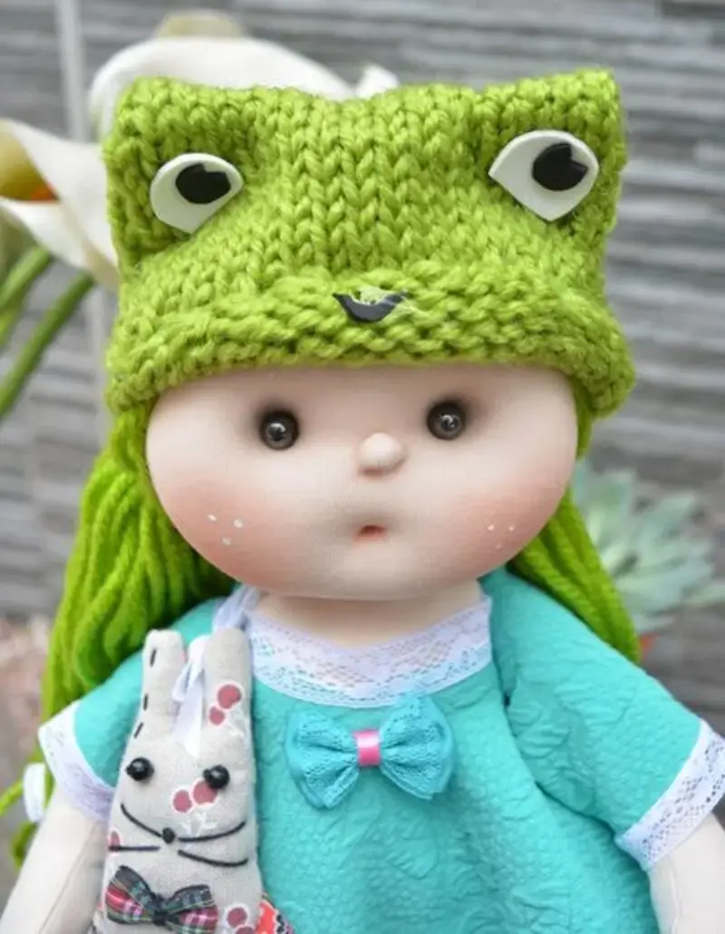 Muñeca de tela artesana Maryxeniss: primer plano con gorro de rana hecho de ganchillo y vestido turquesa.