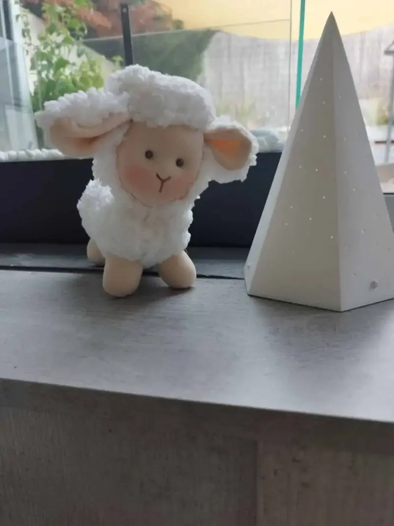 Ovejita de tela artesana de Maryxeniss, complemento hecho a mano junto a una pir&aacute;mide decorativa de tela.