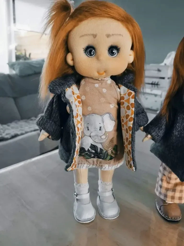 Mu&ntilde;eca de tela artesana Maryxeniss: mu&ntilde;eca con vestido beige de estampado de elefantes, abrigo reversible y calcetines blancos con puntilla.