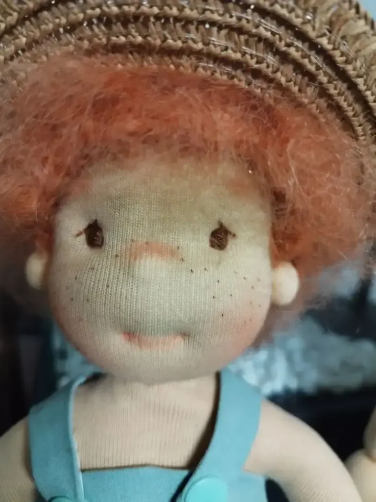 Mu&ntilde;eca de tela artesana Maryxeniss inspirada en Tom Sawyer: primer plano de mu&ntilde;eco con pelo rizado, sombrero de paja y peto.